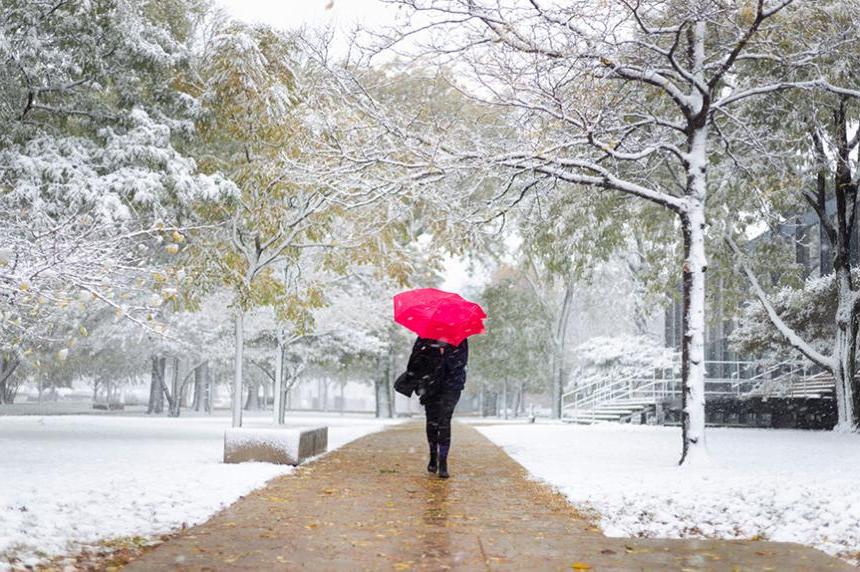 A student walking in the snow on Mies Campus carrying a red umbrella